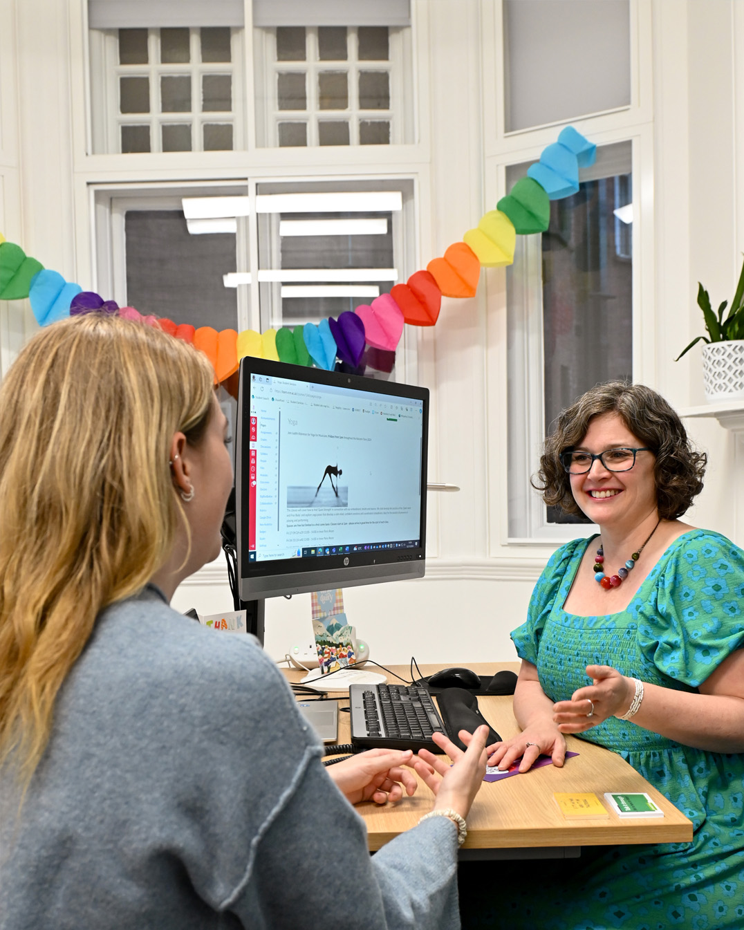 A women with brown hair, talking to a student with blonde hair, smiling.